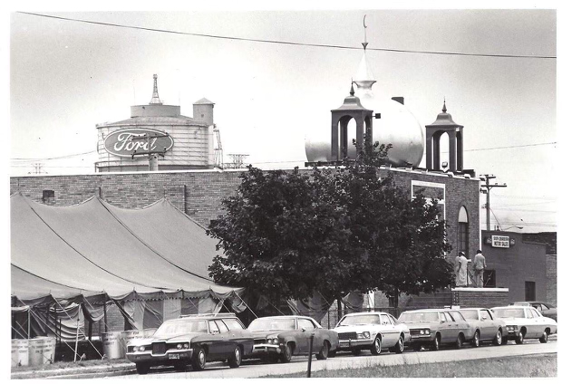 Black and white photo of the AMS building with its silver dome, the Ford Rouge Plant tower with the Ford logo visible in the background