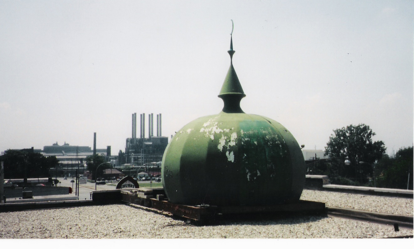 View of the AMS green dome from the building's rooftop, with factory smokestacks visible in the distant background, a powerful image of faith amid industry